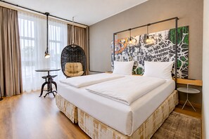 A hotel room with a large bed, a hanging chair, a small table, and a wall with a cityscape painting. - Seminaris Sunday Hotel Nürnberg (Nuremberg)