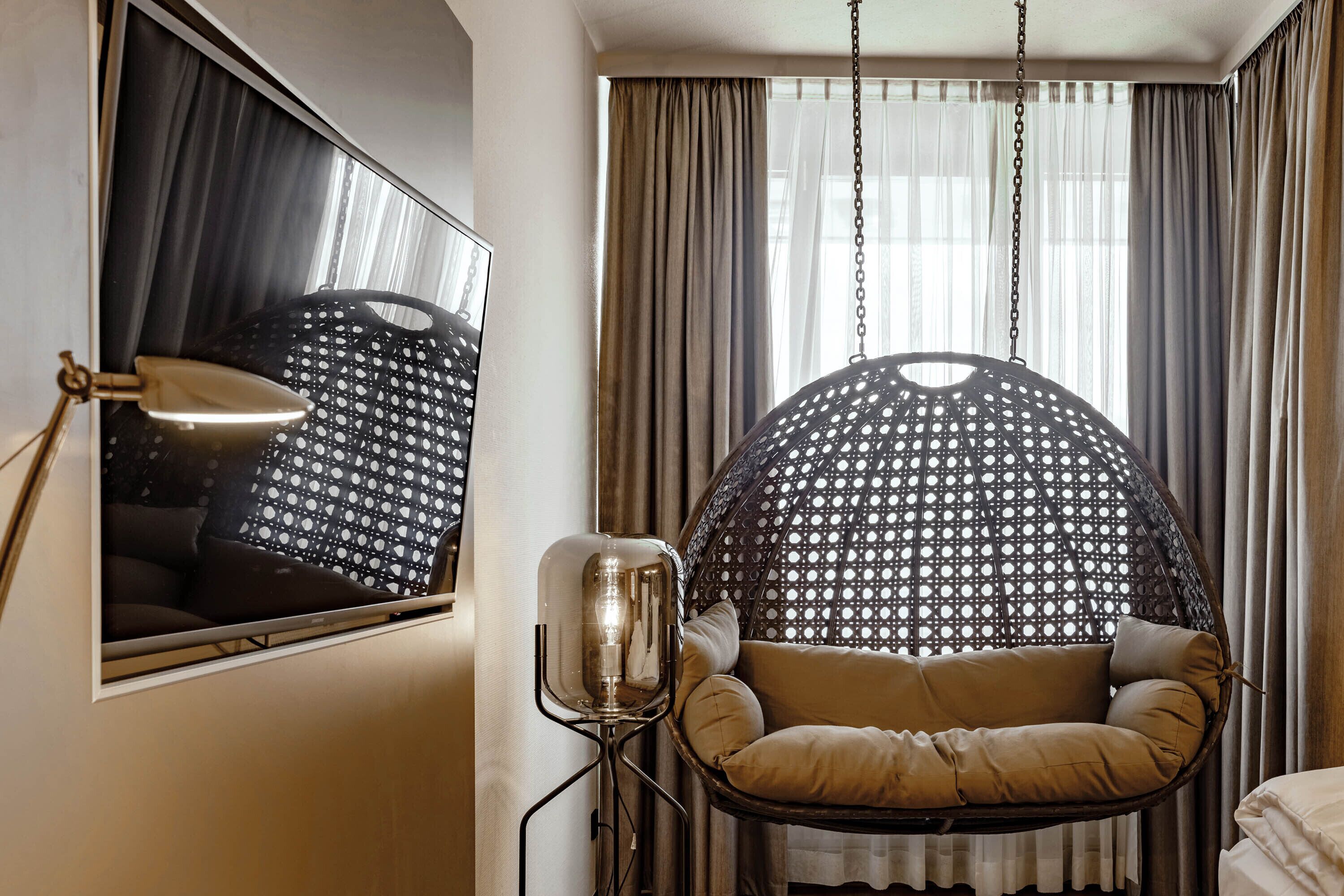 A room with a hanging chair, a floor lamp, and a bed.