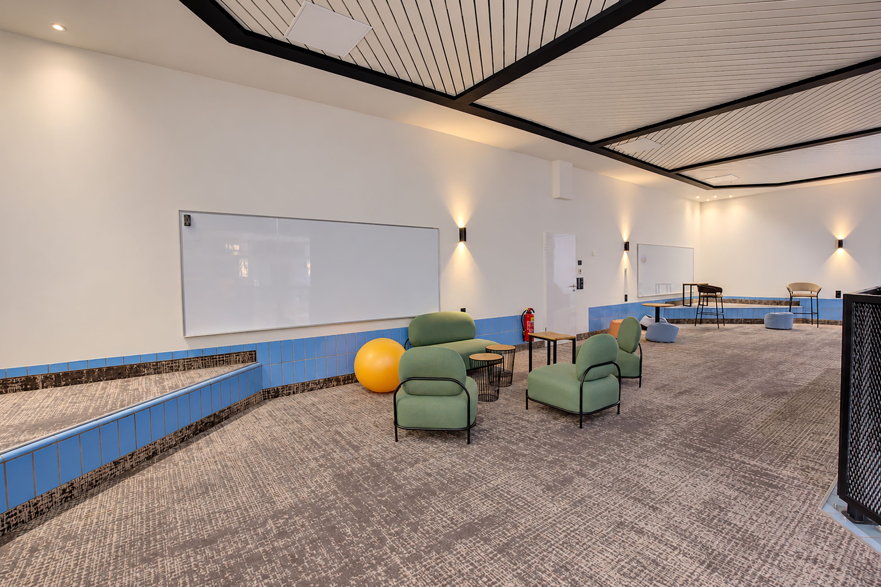 A conference room with a whiteboard, green seating, a small table, and a fire extinguisher.
