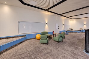 A conference room with a whiteboard, green seating, a small table, and a fire extinguisher.