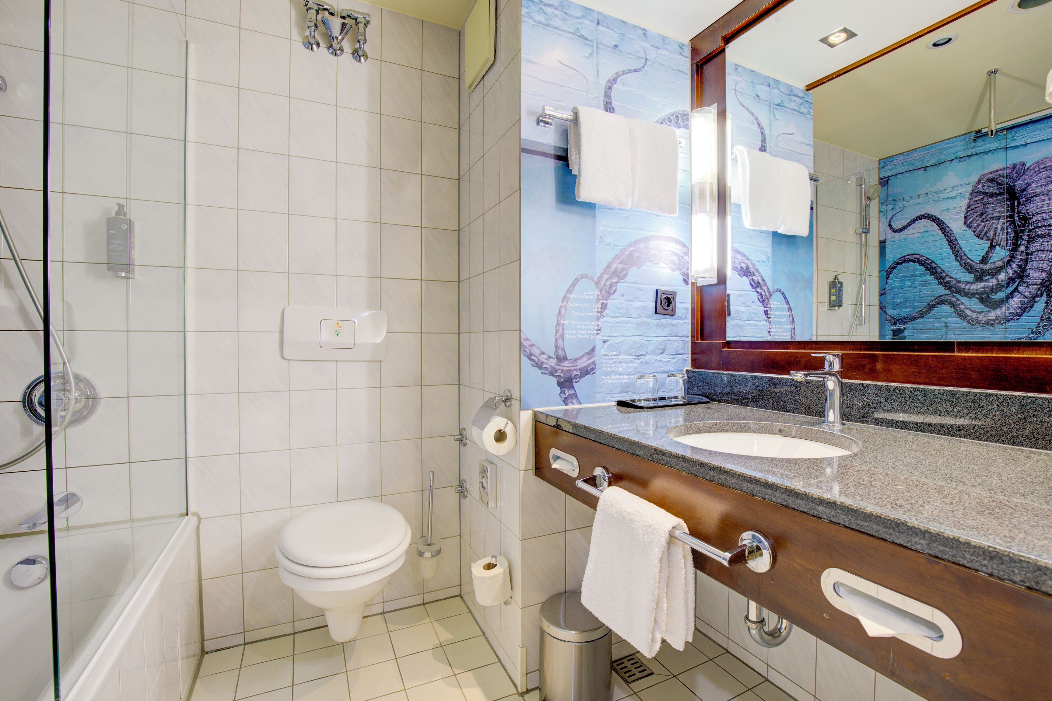 Un baño con inodoro, ducha, lavamanos con espejo y toallero.