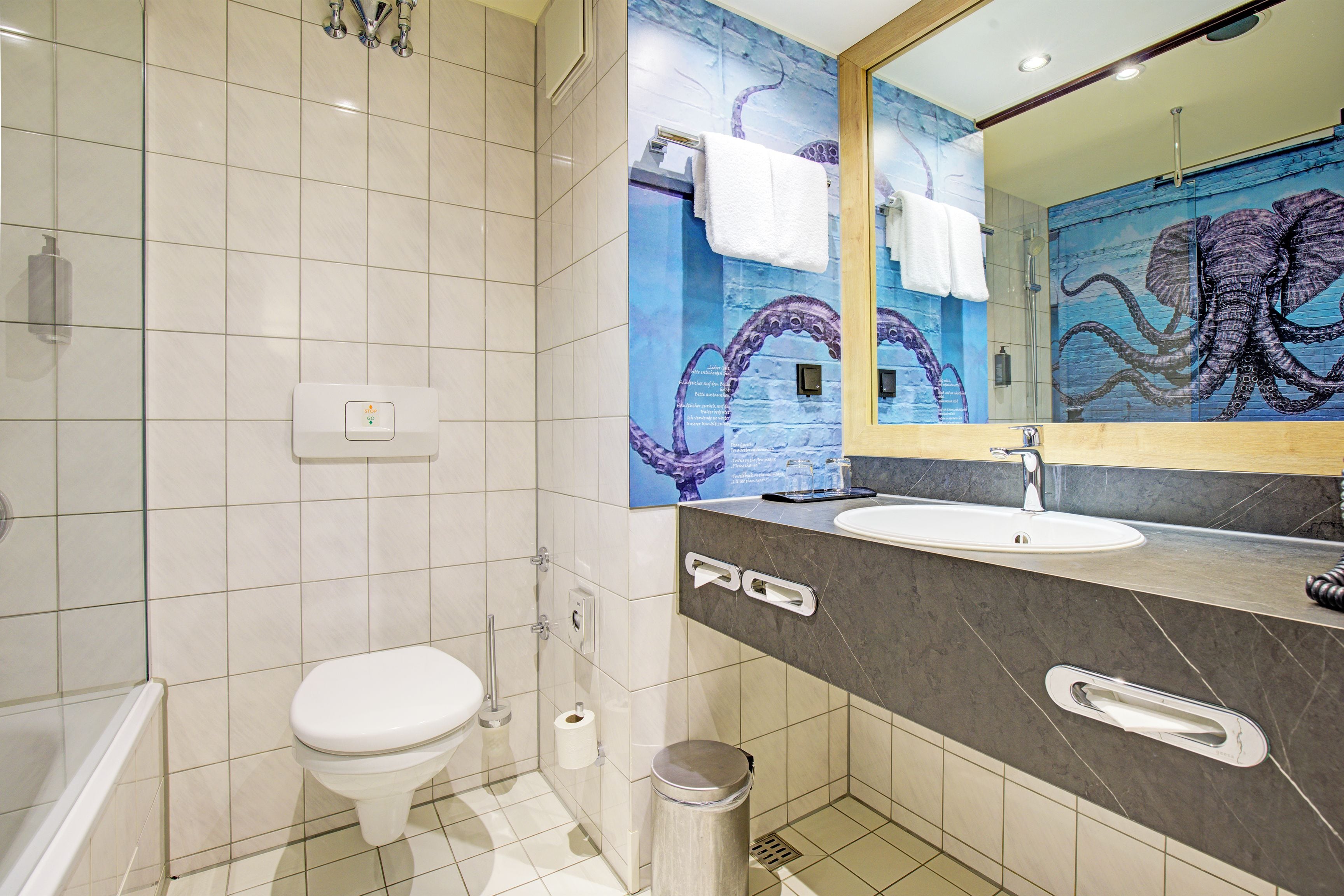 Ein Badezimmer mit Toilette, Waschbecken und Spiegel mit einer Tintenfisch-Wandmalerei.