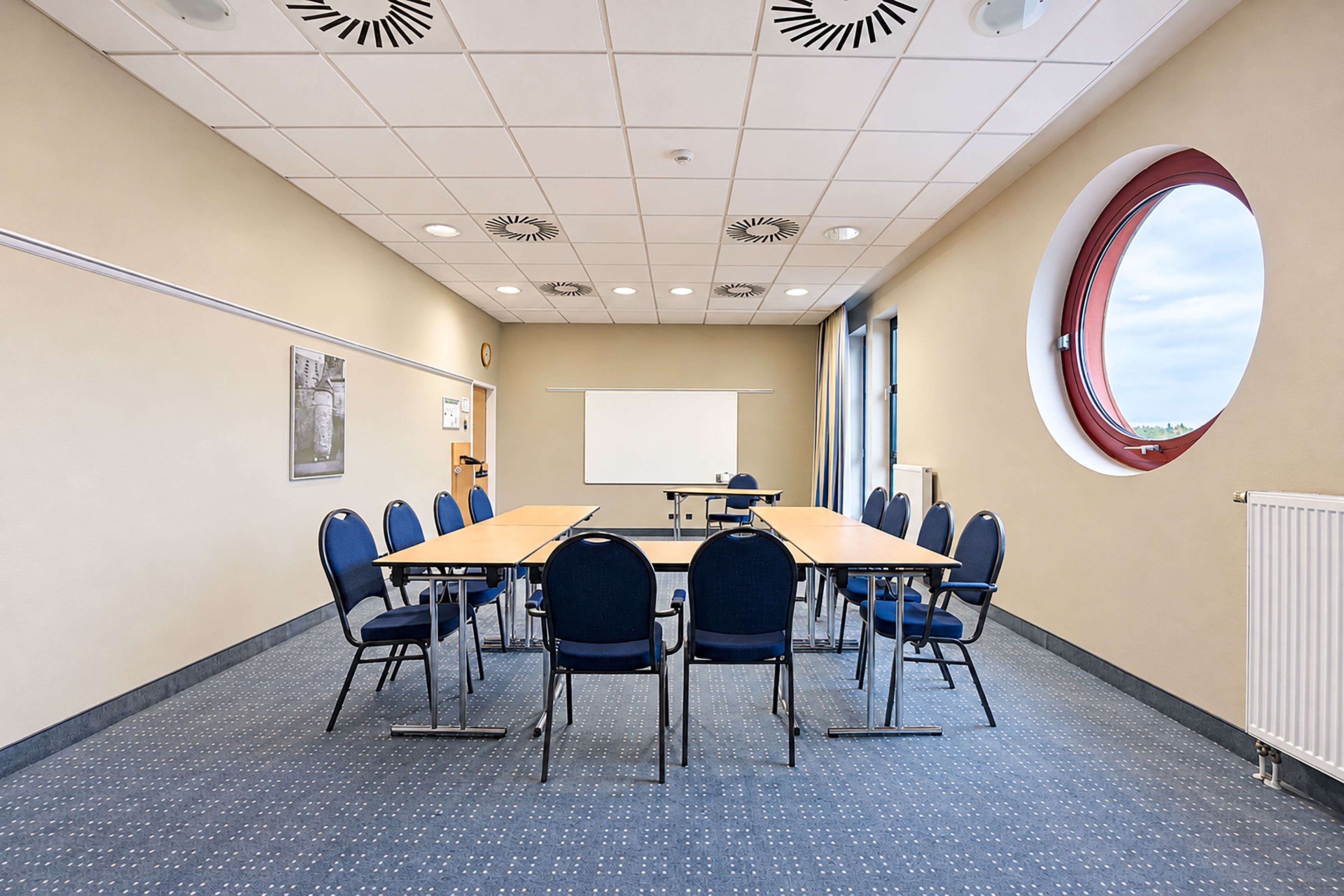 Una sala de conferencias con una gran mesa, sillas, una pantalla de proyector y un amplio ventanal.