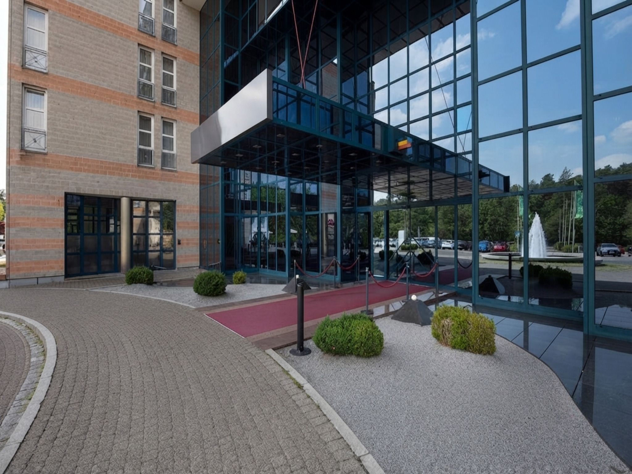Ein modernes Gebäude mit Glasfassade, einem roten Teppich und einem Parkplatz mit Autos.