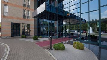 Ein modernes Gebäude mit Glasfassade, einem roten Teppich und einem Parkplatz mit Autos.