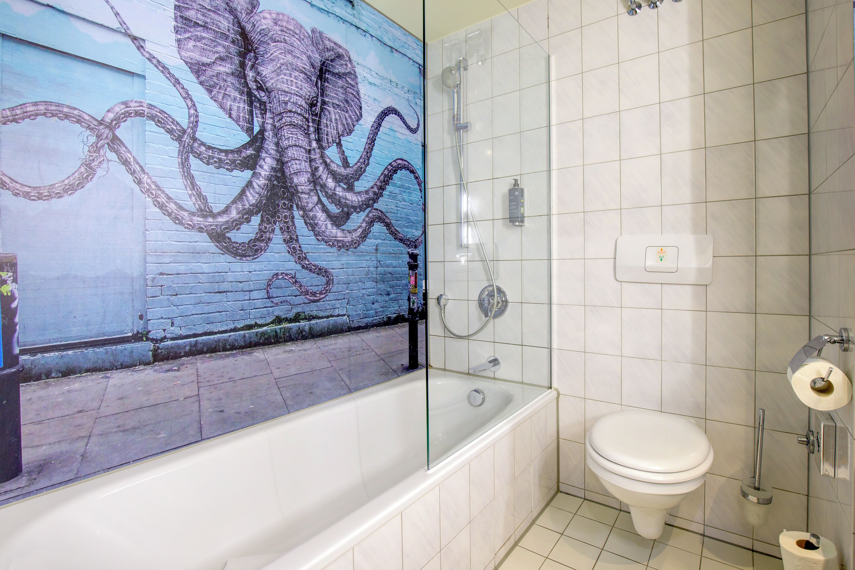 A bathroom with a white toilet, a glass shower enclosure, and a wall-mounted soap dispenser.