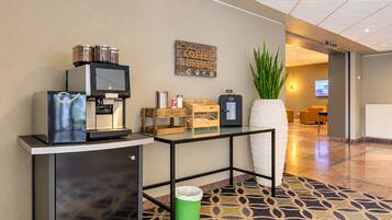 A hotel lobby with a coffee station, a waste bin, a potted plant, and a reception desk.