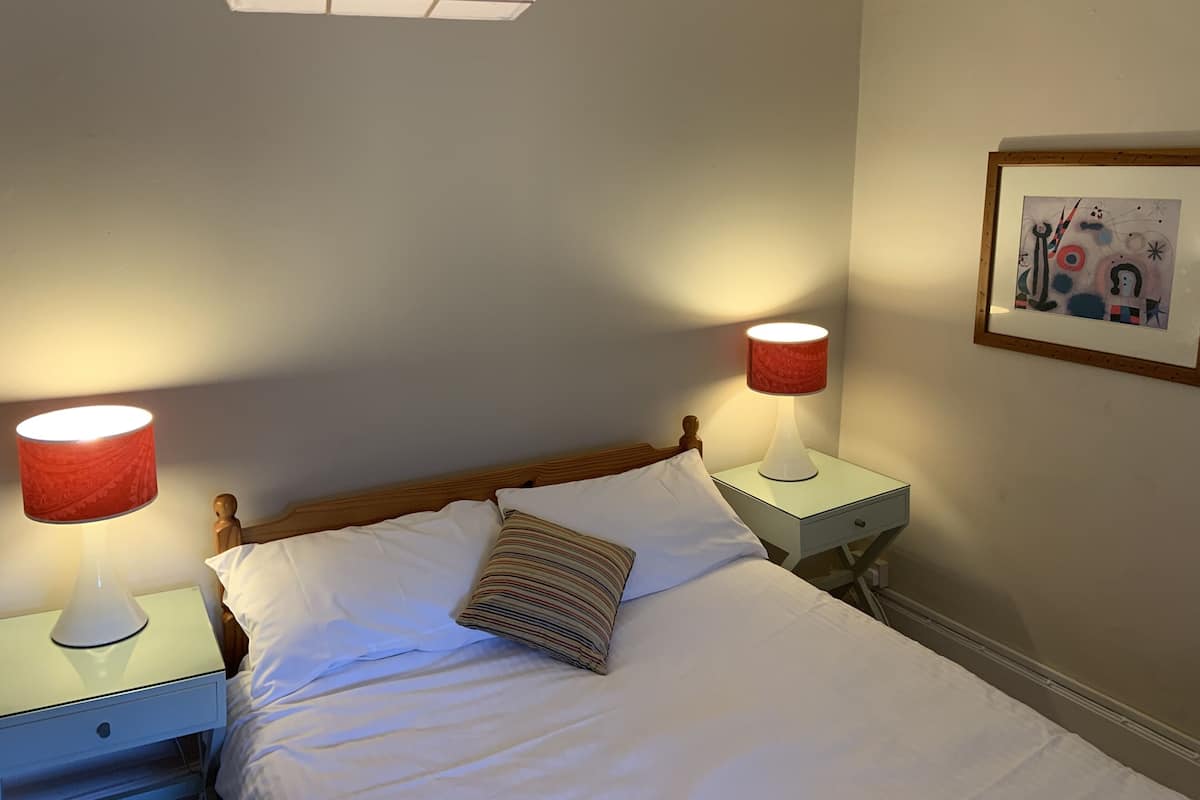 A neatly made bed with white linens and two bedside lamps with red shades.