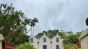 A colonial-style building with a symmetrical facade, arched doorways, and a central entrance flanked by red gates. - Giggles - Beautiful Bajan Villa with Private Pool (Sunset Crest)