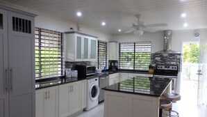A modern kitchen with white cabinets, a built-in washing machine, a large island with bar stools, and a ceiling fan. - Giggles - Beautiful Bajan Villa with Private Pool (Sunset Crest)