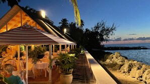A beachfront restaurant with outdoor seating, palm trees, and a view of the ocean. - Giggles - Beautiful Bajan Villa with Private Pool (Sunset Crest)