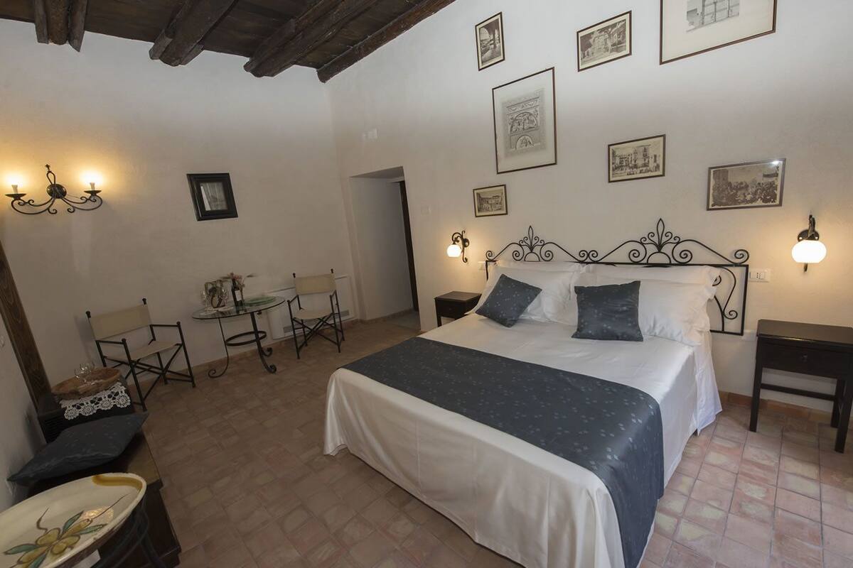 Quarto com cama, duas cadeiras, uma mesa e parede com quadros.