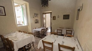 A dining area with multiple tables set for four, each with white tablecloths, wooden chairs, and cutlery.