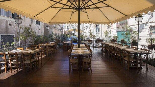 An outdoor dining area with wooden tables and chairs, covered by a large umbrella.