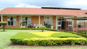 A building with a brick facade, large windows, and a covered outdoor area with chairs. - Kolping Hotel Hoima (Hoima)