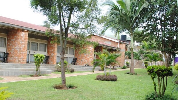 A building with a brick facade, a flat roof, and a small front garden with palm trees and shrubs. - Kolping Hotel Hoima (Hoima)