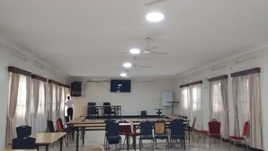 A conference room with tables, chairs, a projector screen, ceiling fans, and curtains. - Kolping Hotel Hoima (Hoima)