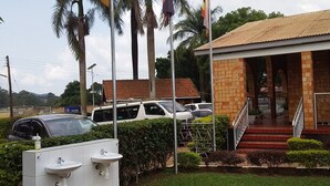 A building with a tiled roof, a staircase leading to the entrance, and a parking area with cars. - Kolping Hotel Hoima (Hoima)