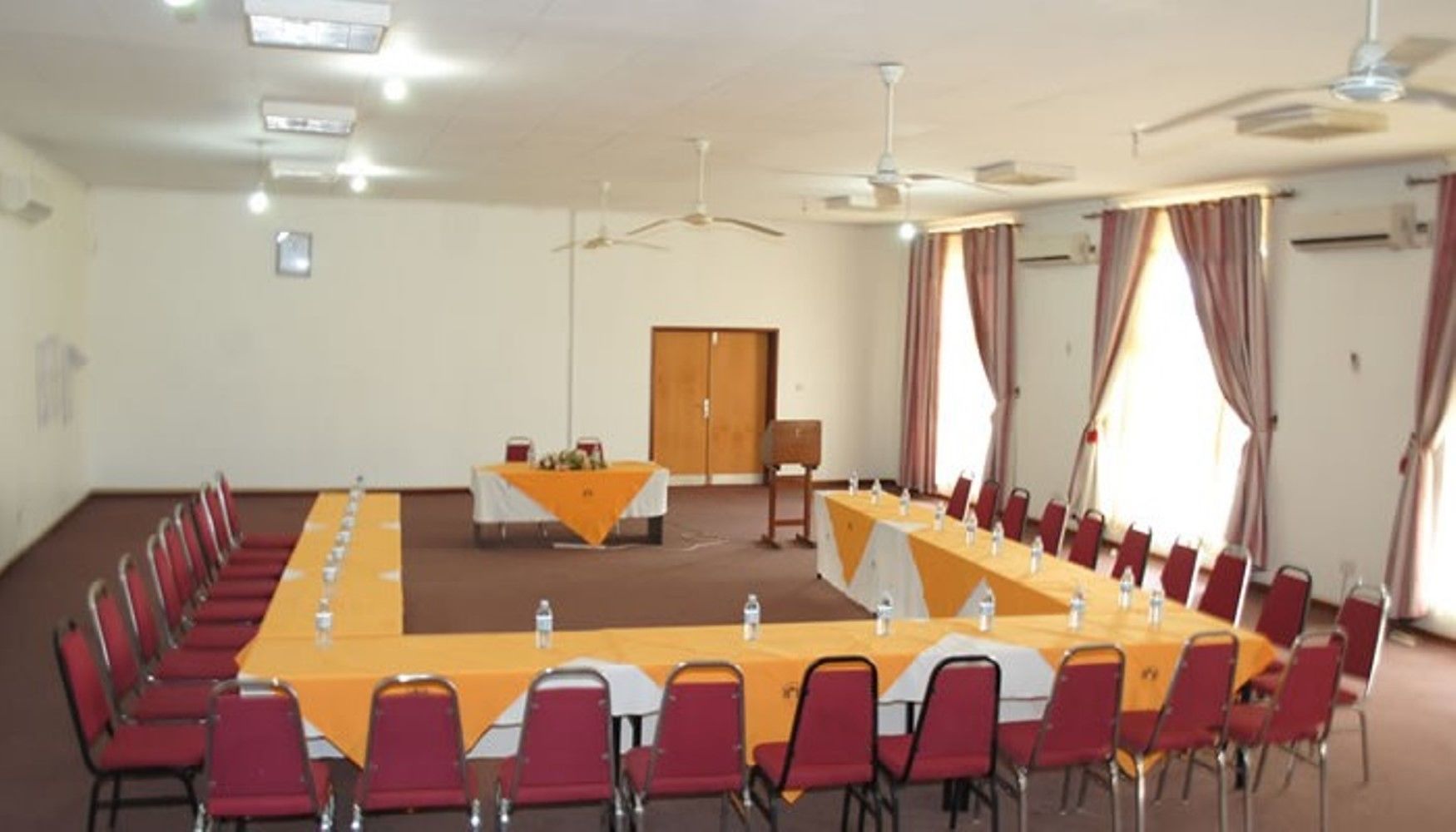 Un salón de conferencias con una larga mesa, sillas rojas y ventiladores de techo.