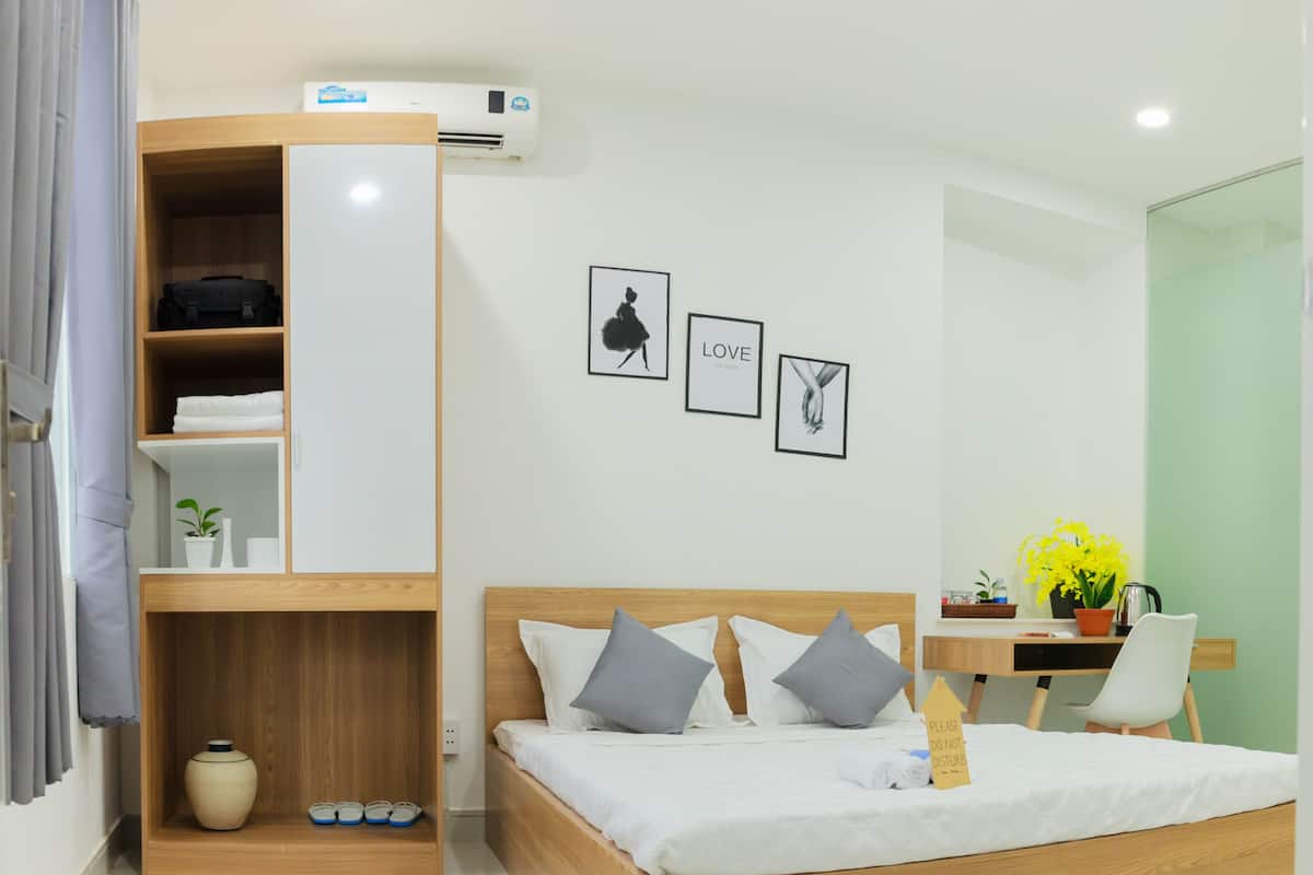 A modern bedroom with a wooden bed, a built-in wardrobe, a small desk, and a potted plant.