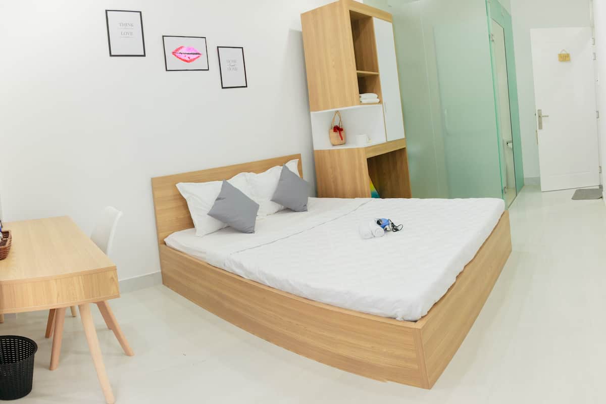 A modern bedroom with a wooden bed, a small wooden desk, and a glass door leading to another room.