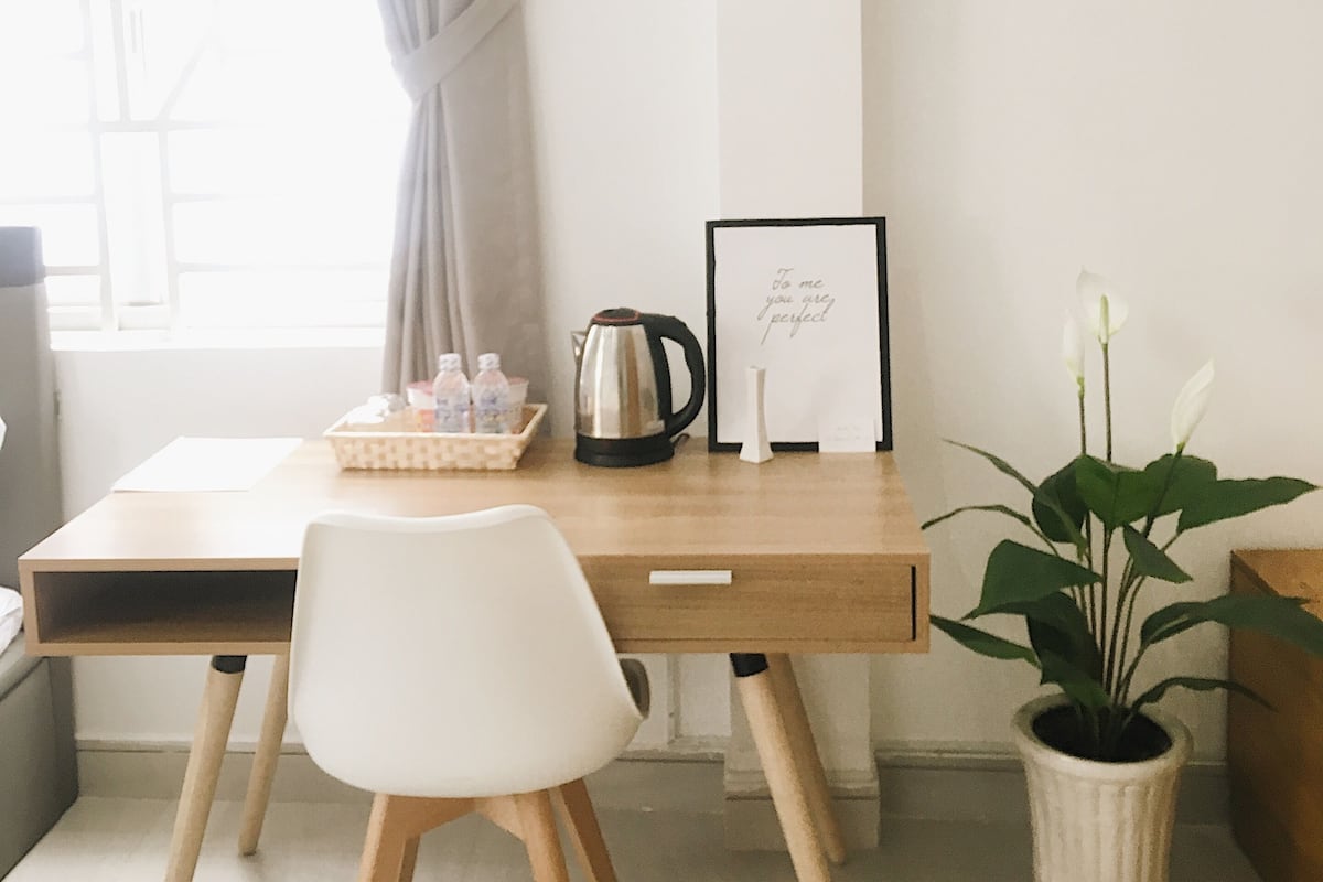 A minimalist office space with a wooden desk, a white chair, a potted plant, and a framed inspirational quote.