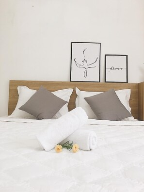 A neatly made bed with white linens, two gray pillows, and a rolled white towel. There are three framed pictures on the wall above the bed, one with a silhouette of a couple and another with the word "dream". - Hello Saigon Homestay (Ho Chi Minh City)