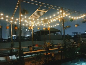An outdoor seating area with string lights and hanging planters, overlooking a cityscape with tall buildings. - Hello Saigon Homestay (Ho Chi Minh City)