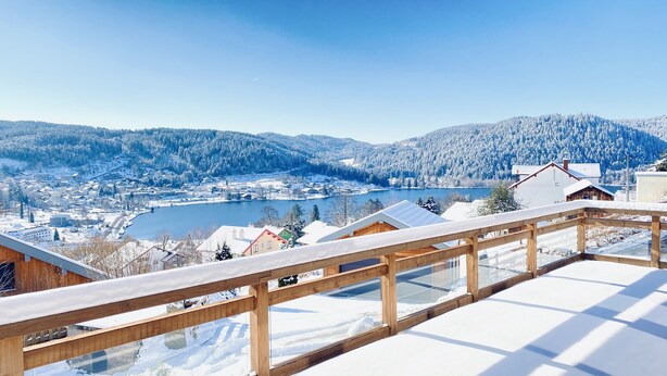 En snötäckt balkong med utsikt över en stad och berg.