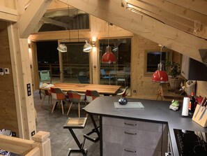 Cozinha moderna com mesa e cadeiras de madeira, bancada preta e luminárias pendentes vermelhas.