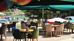 An outdoor cafe with tables and chairs, a view of the water and buildings in the background. - Dilek Suit & Cafe (Çaykara)