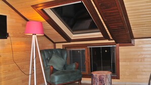 A cozy room with a sloped ceiling, a green leather chair, a round wooden stool, and a floor lamp. - Dilek Suit & Cafe (Çaykara)