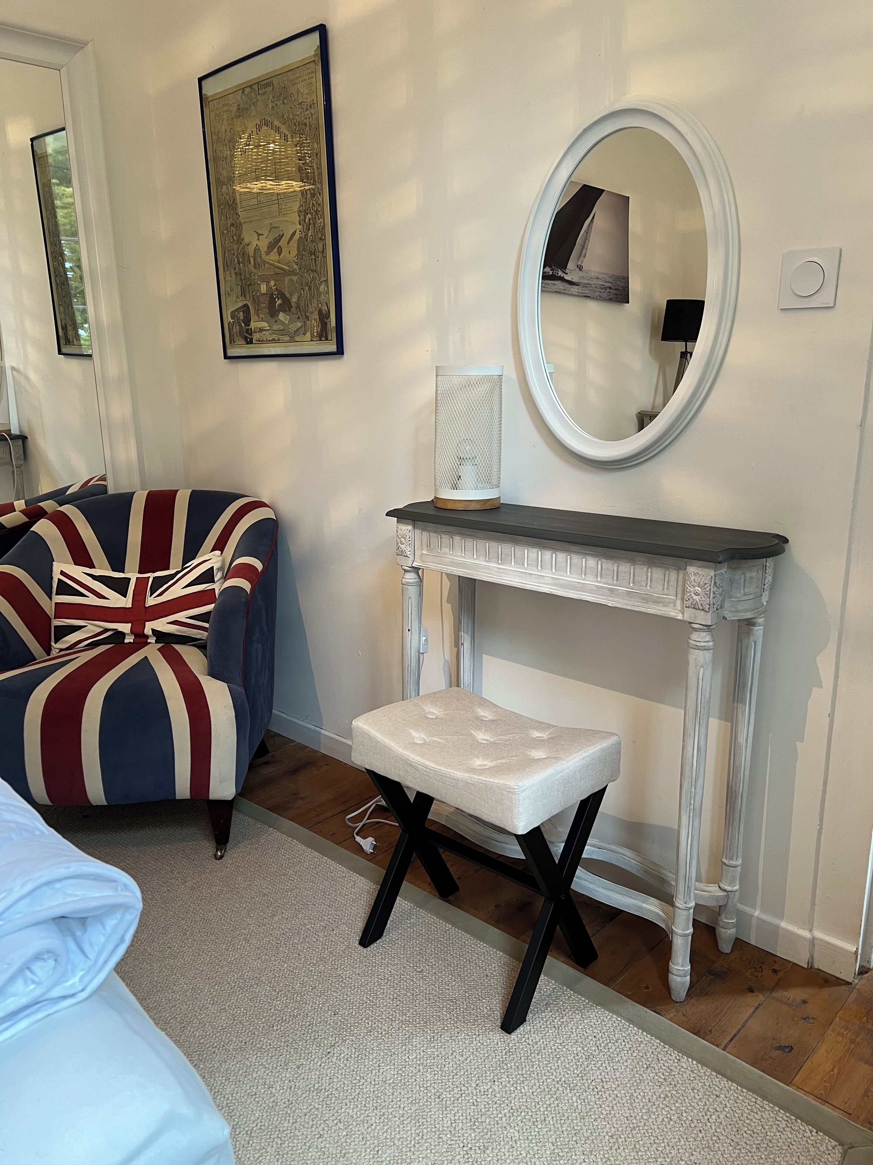 Een kamer met een fauteuil bekleed met een Union Jack, een witte kussenbank, een witte schoorsteenmantel en een ronde spiegel.
