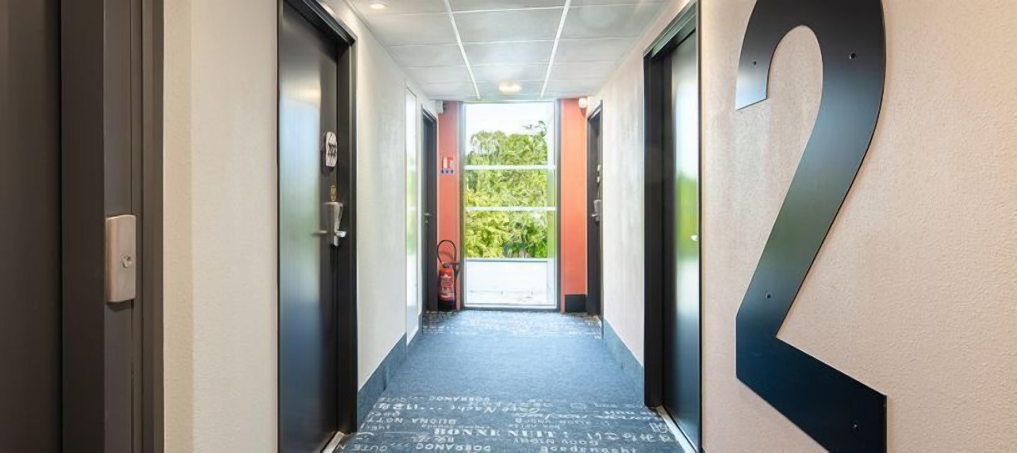 Un couloir avec un tapis noir, un grand chiffre « 2 » noir peint sur le mur et une porte sur la gauche.