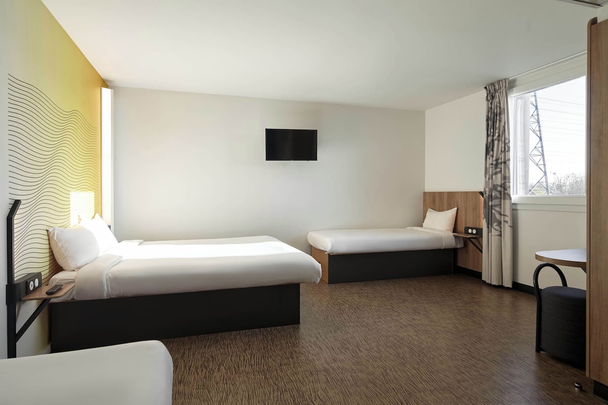 Habitación de hotel con dos camas, un televisor de pantalla plana, una mesita y un ventanal con cortinas.
