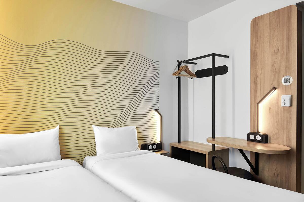 Una habitación de hotel moderna con un diseño de pared ondulado, un aparador de madera, un perchero y una mesita de noche con una lámpara.