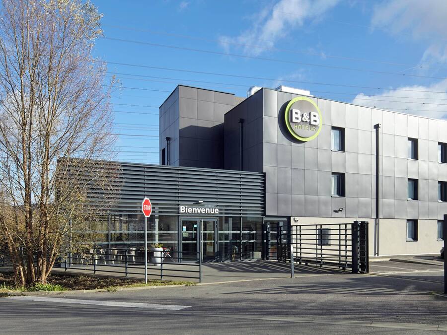 A modern hotel with a 'Bienvenue' sign, a gated entrance, and a clear sky.