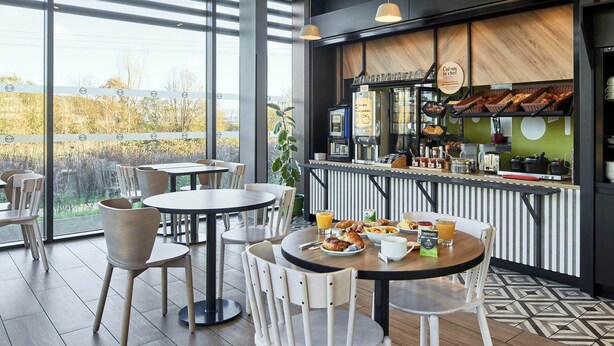 Un café moderno con amplios ventanales, una zona de bar y mesas para los clientes.