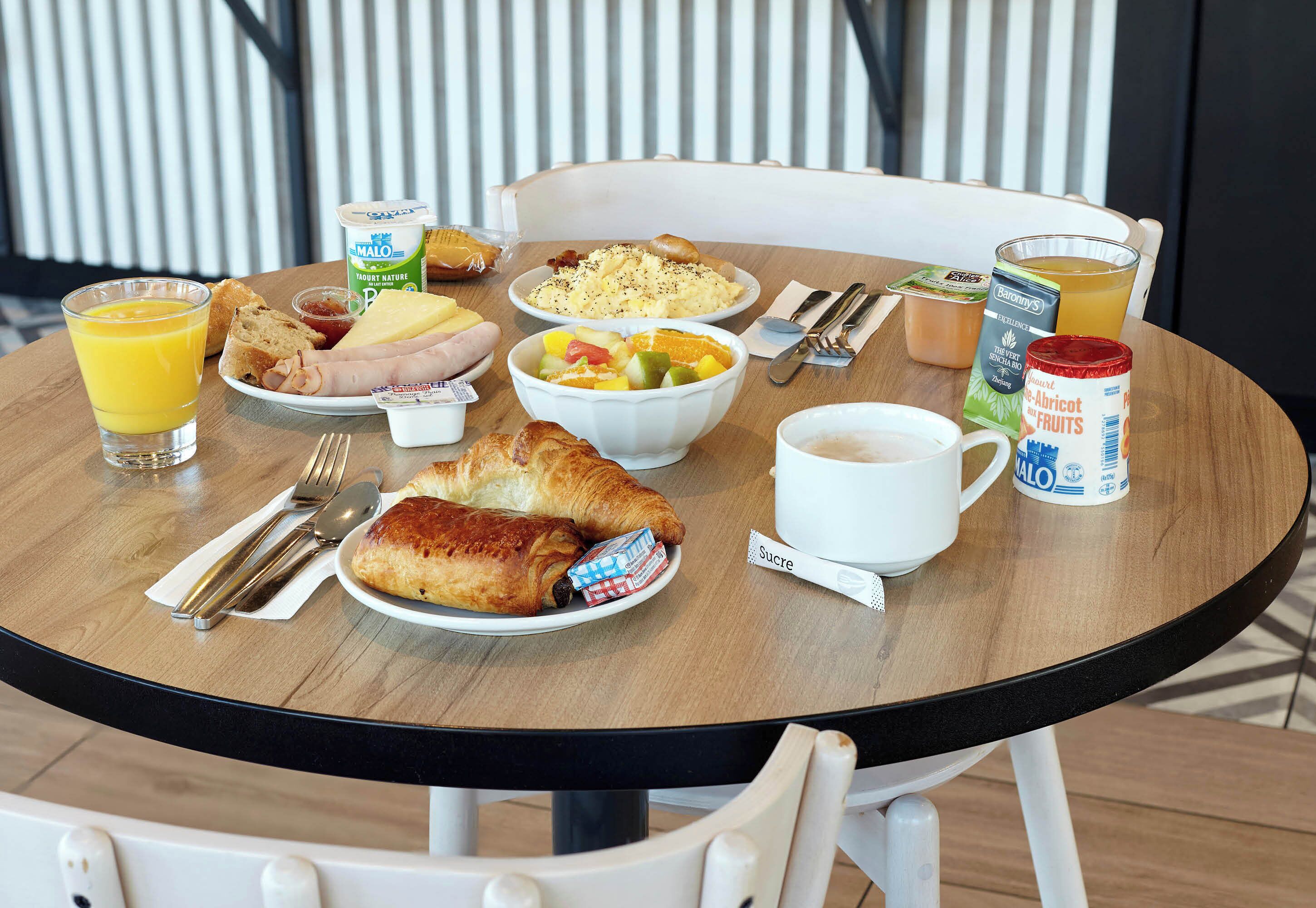 Een ontbijttafel met croissants, fruit, yoghurt en sap.