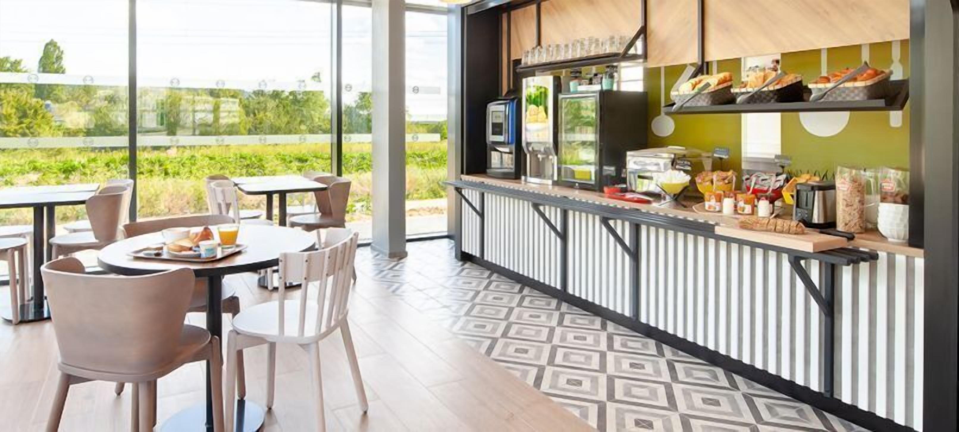 Un café moderne en plein air, doté d’une terrasse, de tables, de chaises et d’un comptoir où l’on sert des plats et des boissons.
