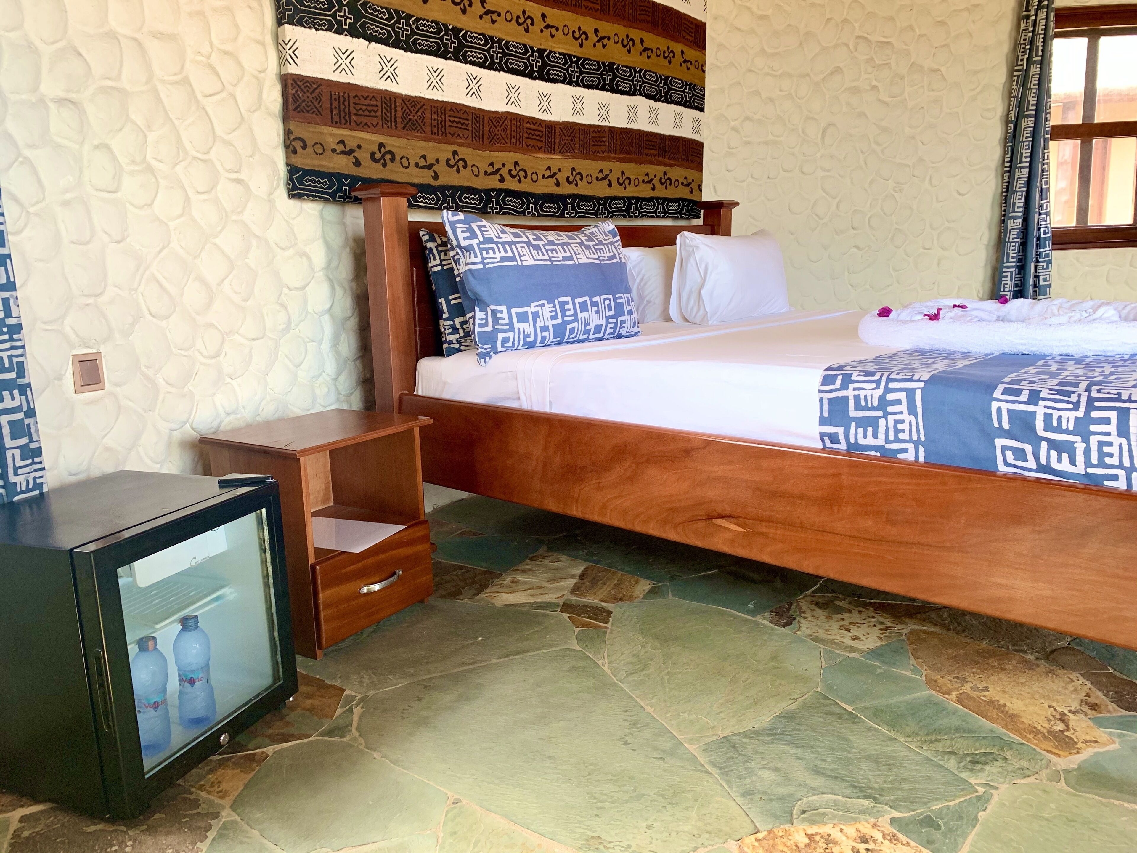 A room with a bed, a wooden nightstand, a small TV, and a patterned headboard.