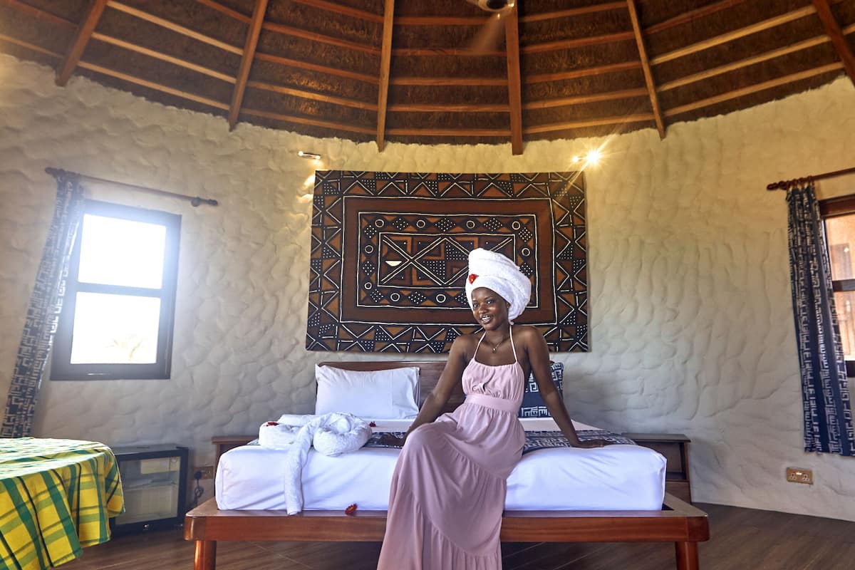 A room with a wooden ceiling, a bed with white linens, a woven basket light fixture, and a patterned tapestry on the wall.