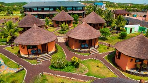 Un resort con cabañas de techo de paja dispuestas en un patrón circular, rodeado de jardines cuidados y palmeras.