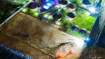 An aerial view of a resort with multiple round-roofed structures, a swimming pool, and a large sandy area.