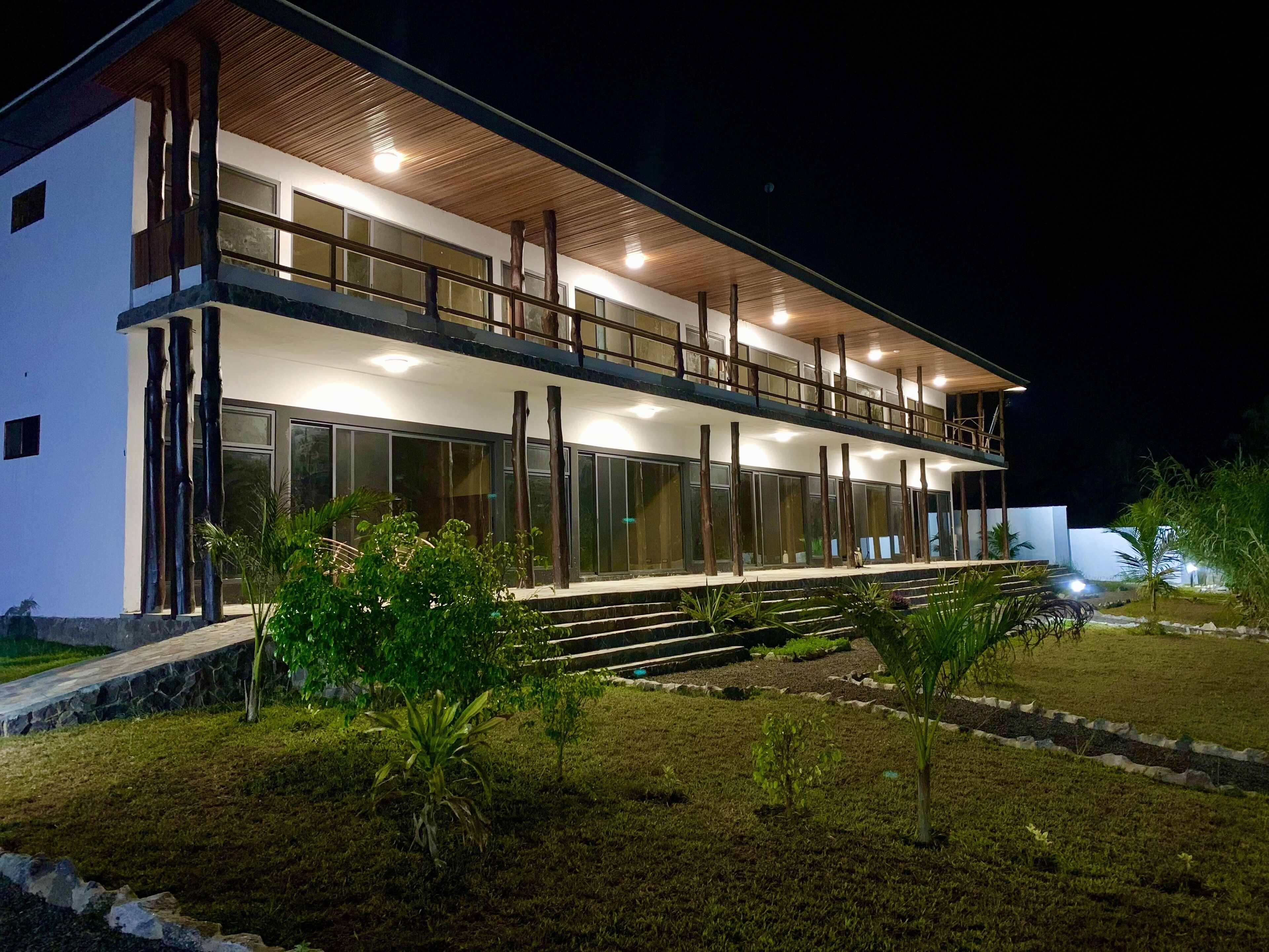 Un edificio moderno de dos pisos con balcón, ventanas grandes y fachada bien iluminada.