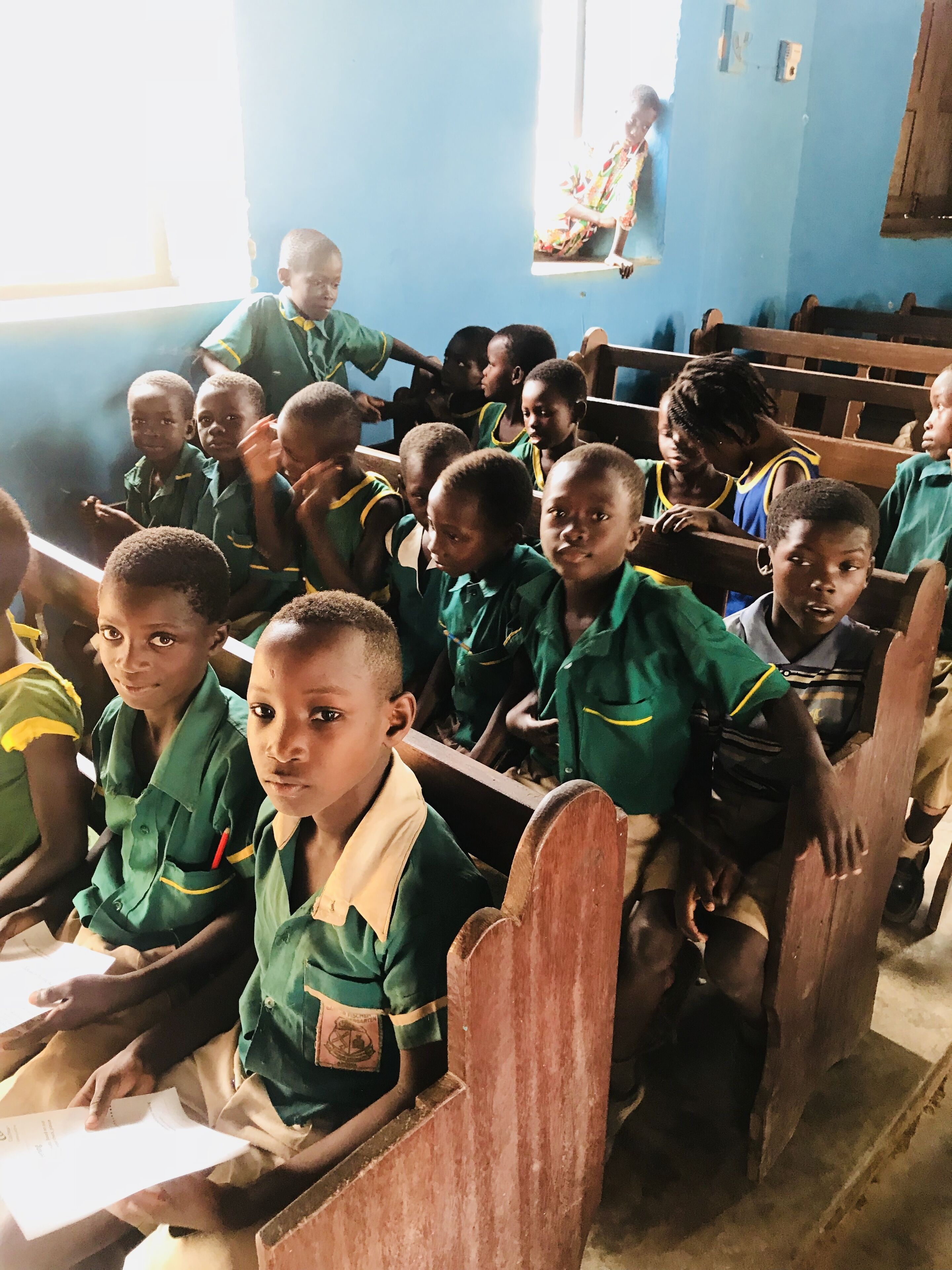 A classroom with students seated at wooden desks, facing a teacher.