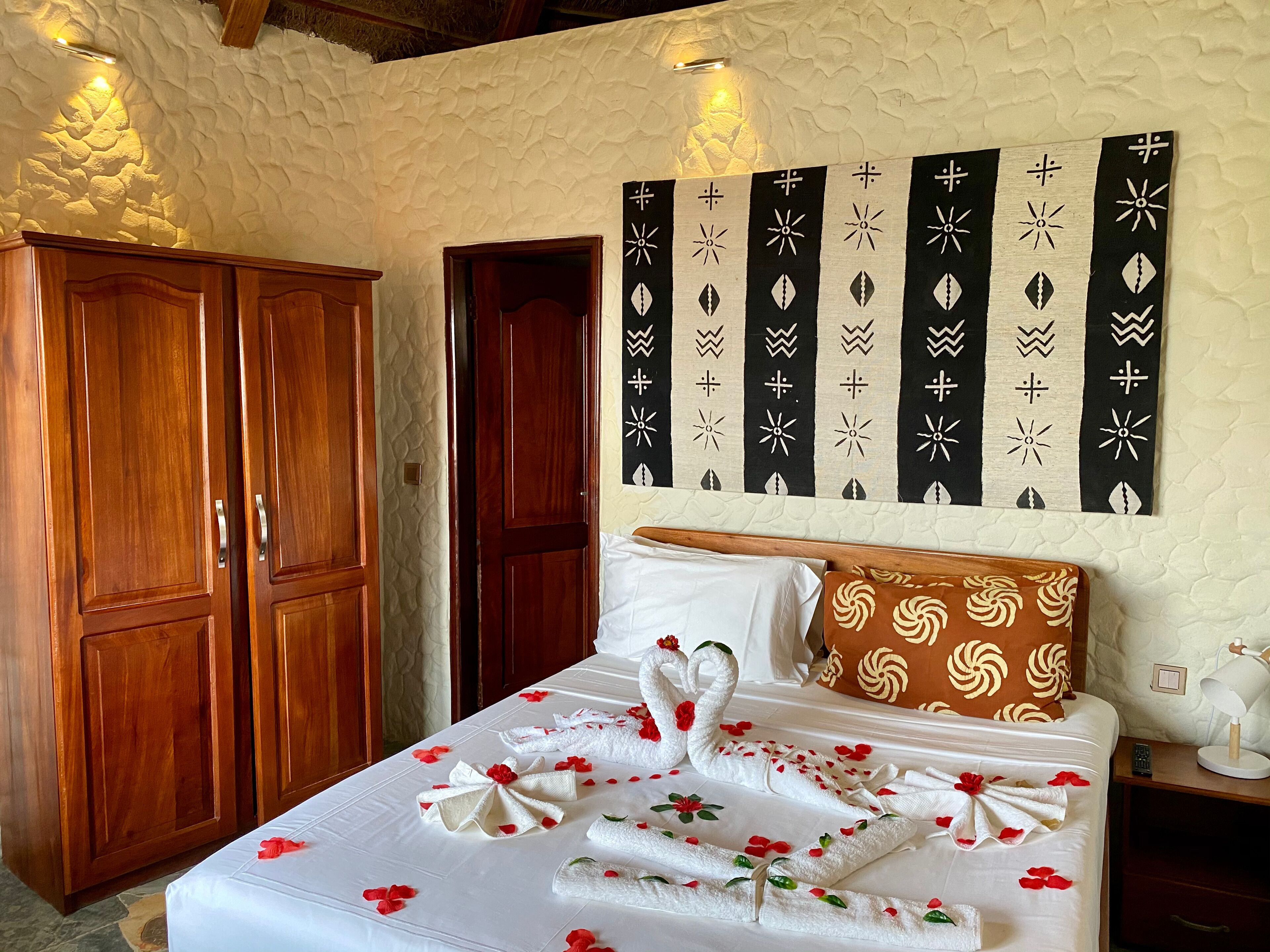 A neatly made bed with towels and flowers, wooden wardrobe, and a wall with decorative panels.