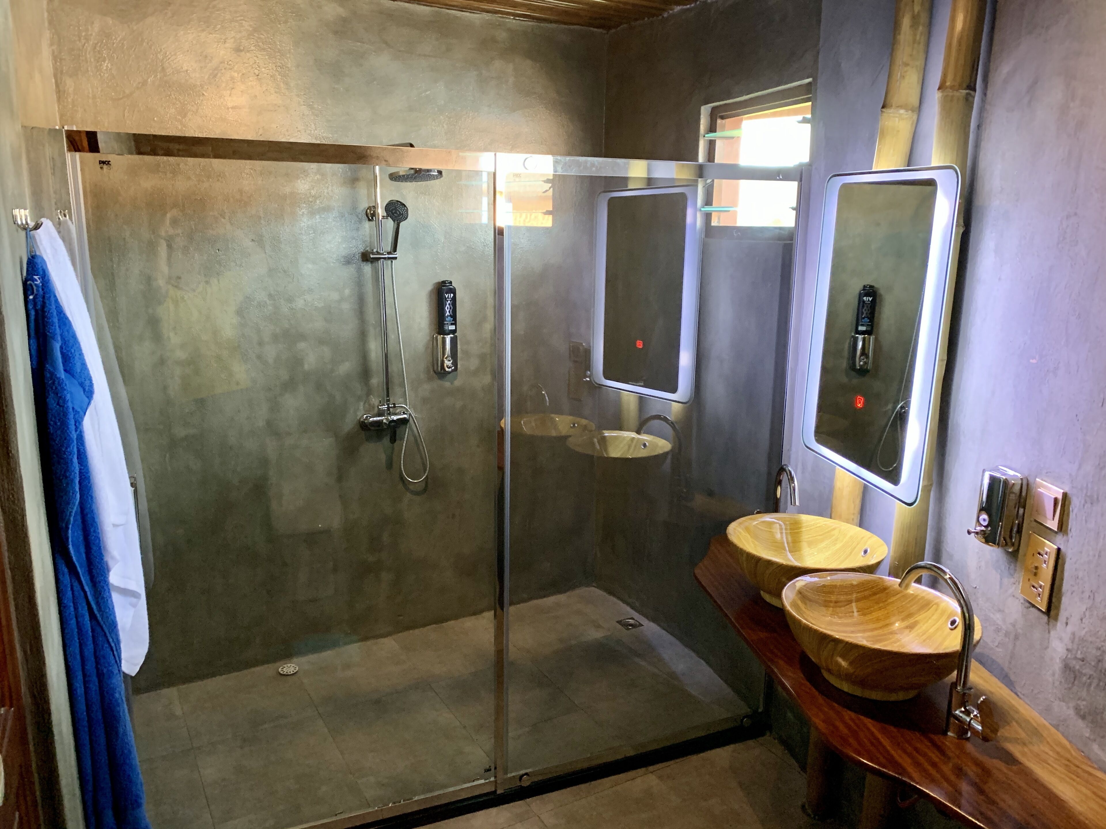Un baño moderno con ducha envuelta en vidrio, dos lavamanos con cuencos de madera y un espejo grande.