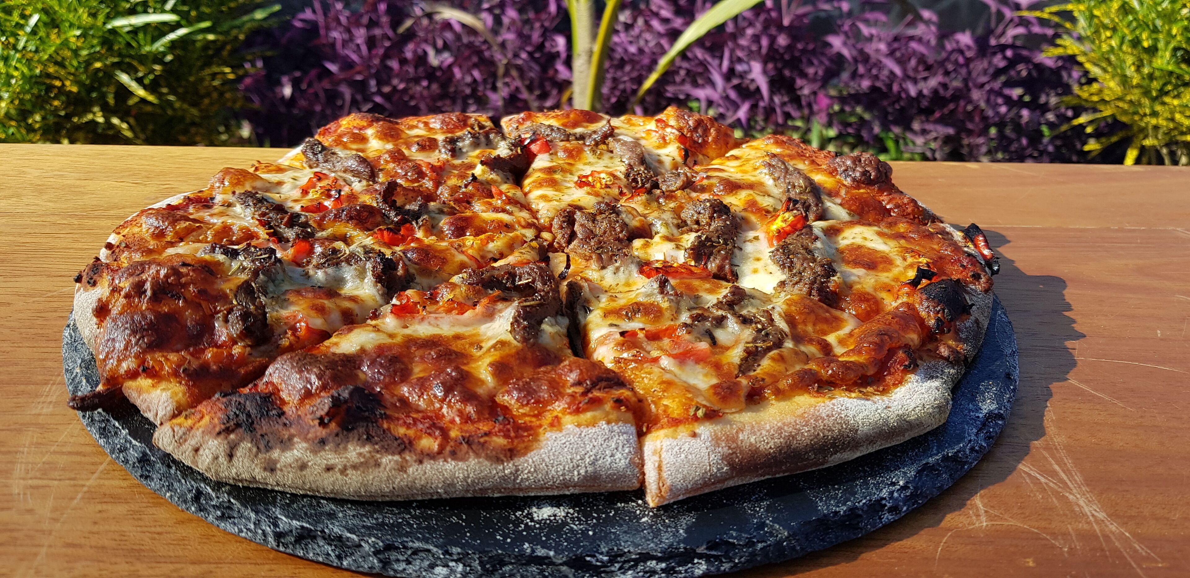 En pizza på en rund, sort skiferplade på et træbord.
