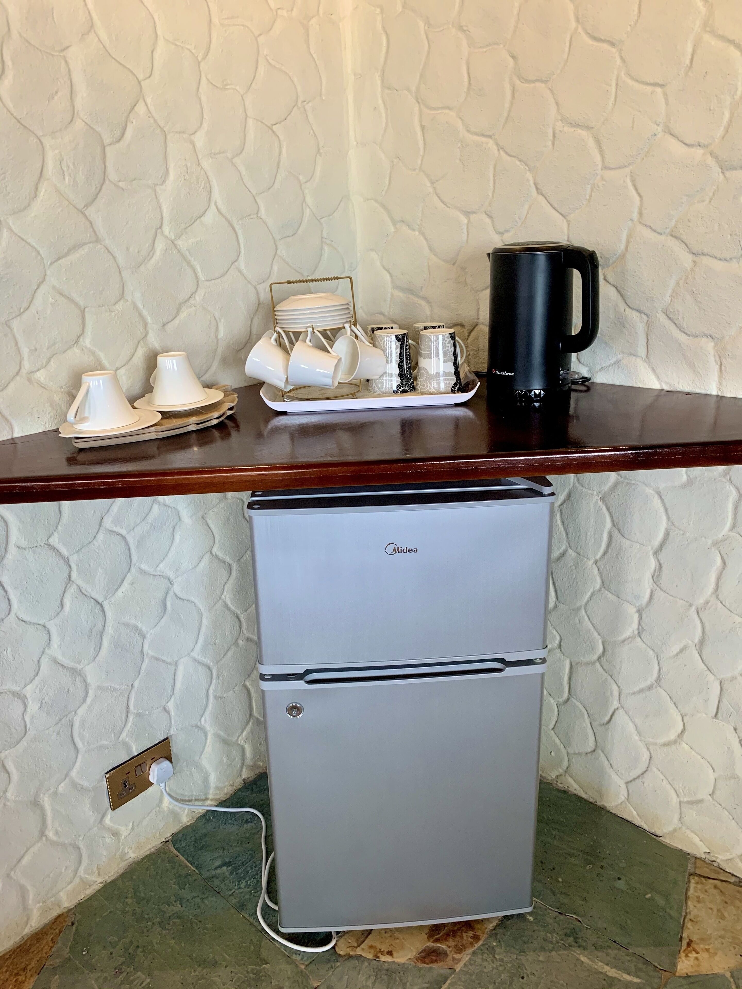 A kitchenette with a small refrigerator, a coffee maker, and a tray with cups and plates.